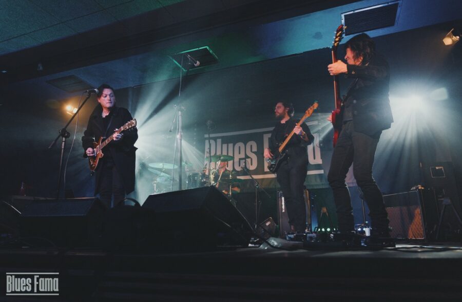 Trzec mężczyzn z gitarami i perkusista grają koncert na scenie w klubie.
