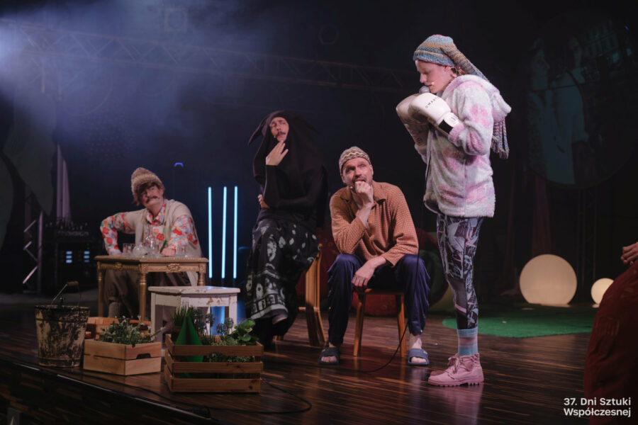 Grupa aktorów na scenie, obok skrzynki z sadzonkami