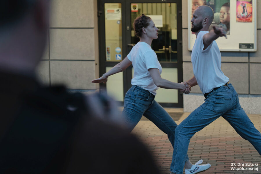 Dwoje performerów wykonuje performans "Stretching" przed budynkiem BOK-u, tańczą.