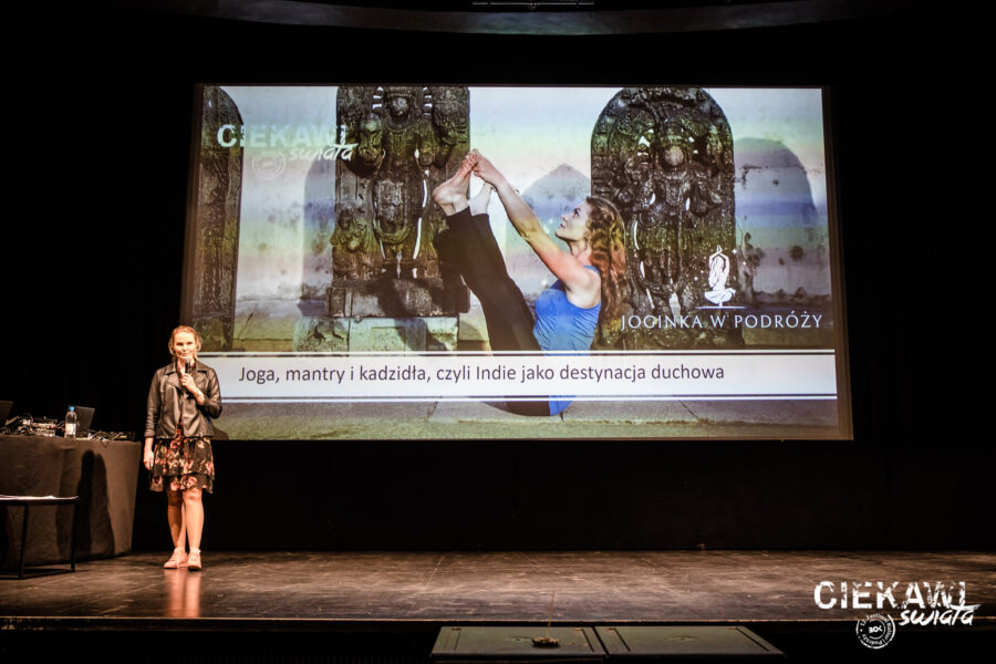 Zdjęcie: kobieta na scenie mówi do mikrofonu, z tylu na ekranie kina wyświetlane są slajdy